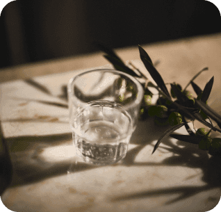 copo com um pouco de agua em cima de uma mesa com um ramo de oliveira ao lado